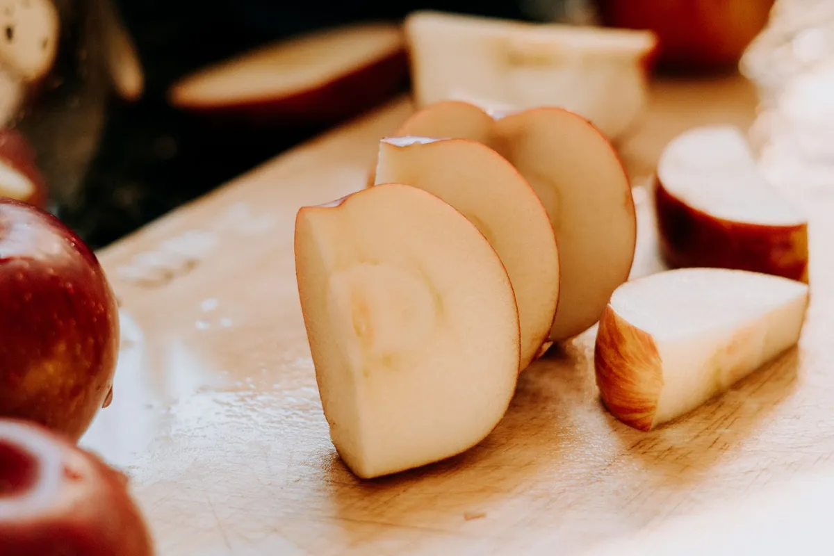 Aufgeschnittene Apfelscheiben und Apfelstücke liegen auf einem Holzbrett, daneben rote Äpfel.