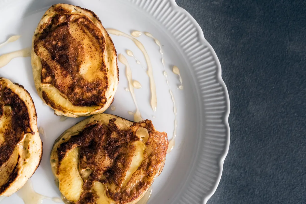 Pfannkuchen mit gebratenen Apfelscheiben und Zimt auf weißem Teller, mit etwas Sirup beträufelt