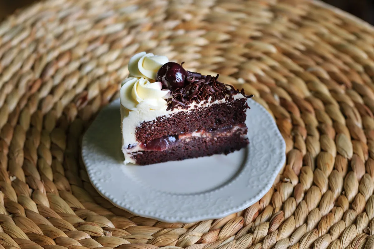 Ein Stück Schwarzwälder Kirschtorte mit Sahne, Schokoladenraspeln und Kirsche auf einem weißen Teller.