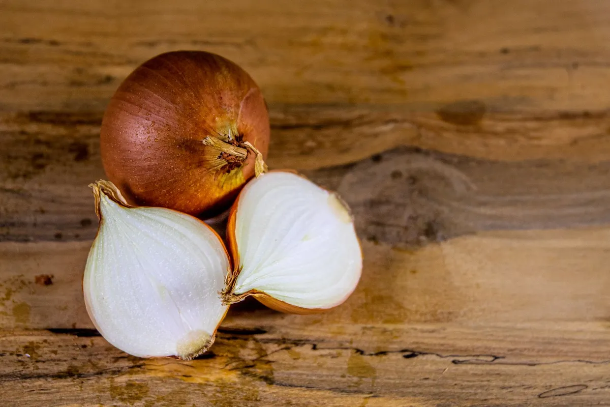 Zwei halbierte und eine ganze gelbe Zwiebel liegen auf einer rustikalen Holzfläche.