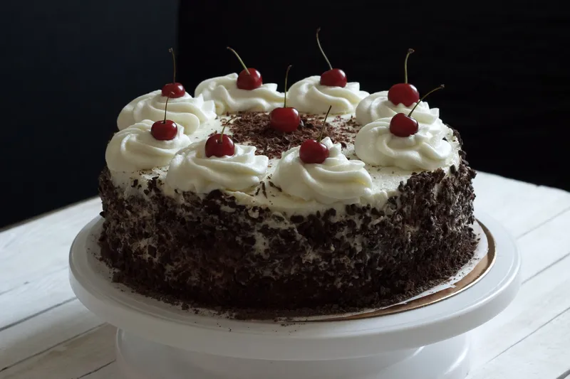Torte mit Sahnetupfen, frischen Kirschen und Schokoladenspänen am Rand auf einer weißen Tortenplatte